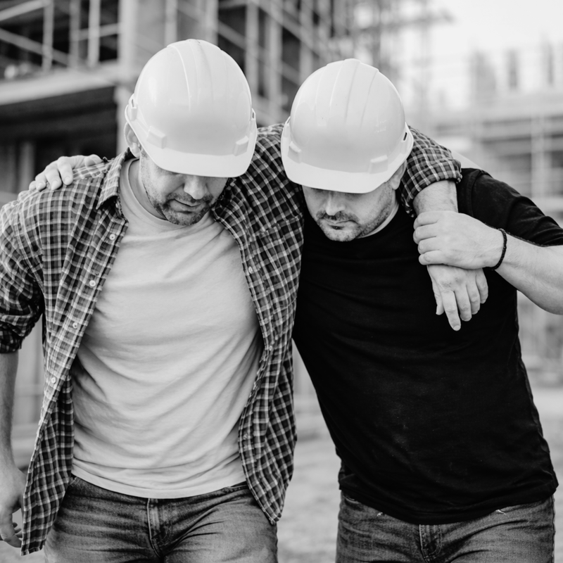 Two men in hard hats embracing each other outdoors.