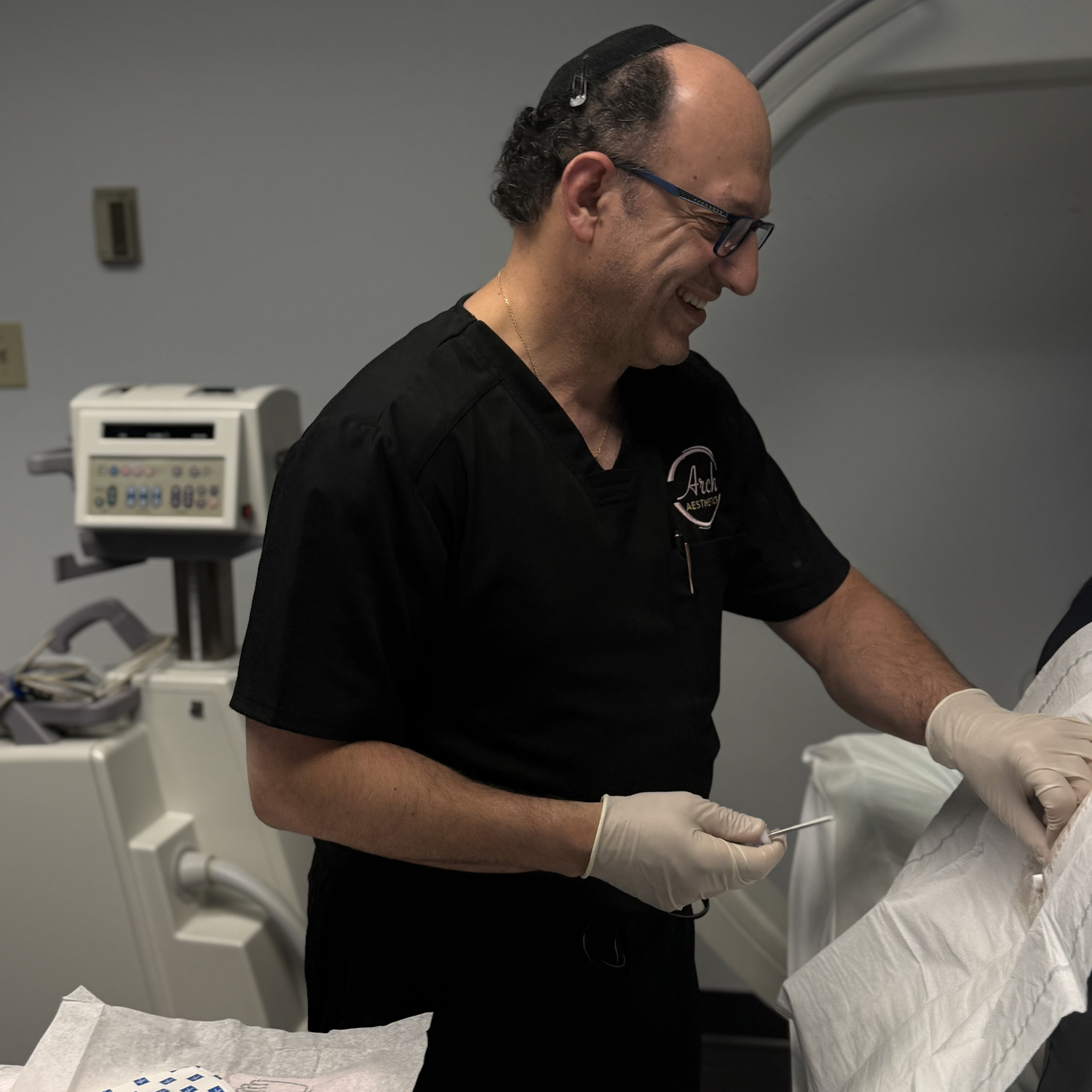 Doctor in black scrubs with a logo performing surgery in an operating room.