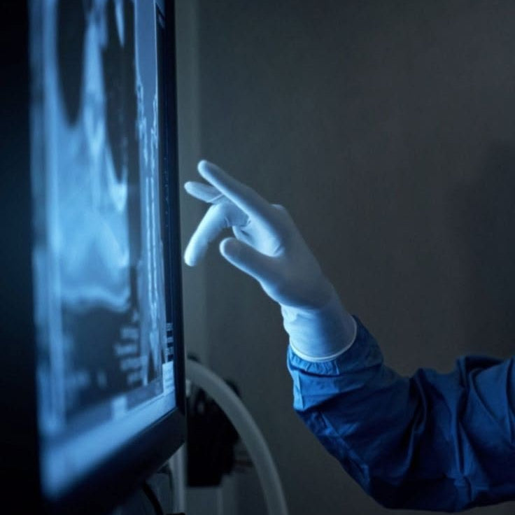 Person in a lab coat and gloves interacting with a medical imaging screen.
